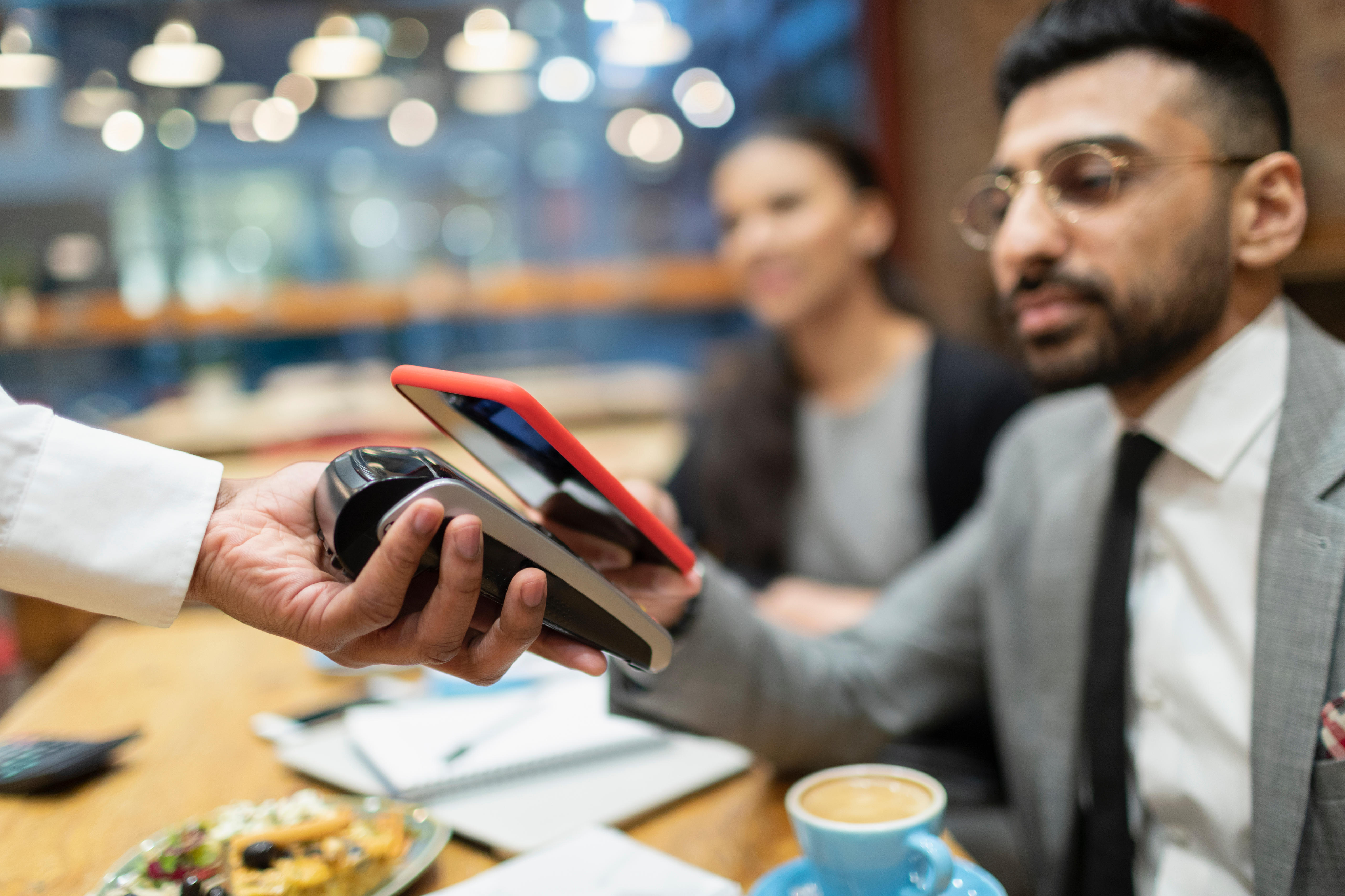 Businessman paying with smartphone at a cafe.