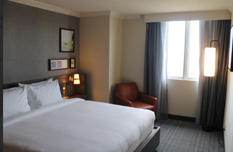 A hotel room with a bed, a leather chair and small art on the walls.