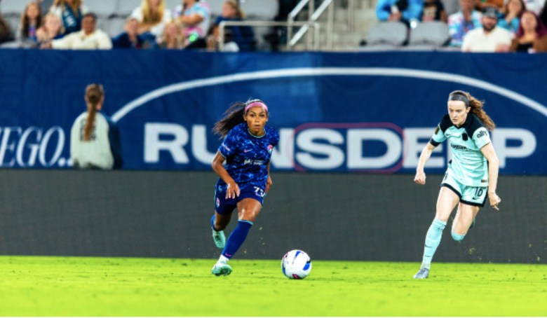 Two soccer players on the pitch, one for tWave FC, the other, giving chase, for Gotham FC.
