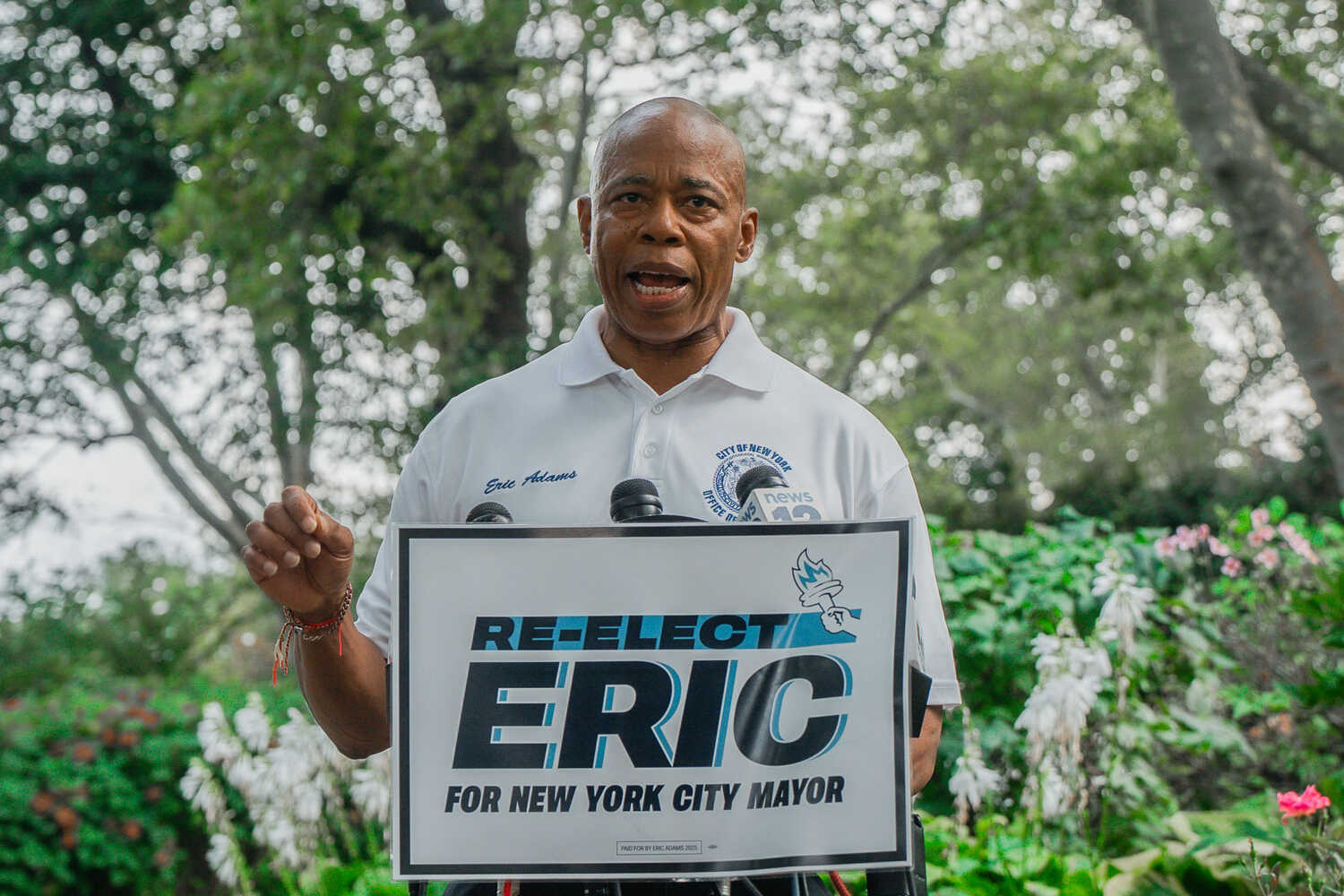 Mayor Eric Adams speaks at an outdoors news conference in New York, standing behind a “Re-elect Eric for New York City mayor” sign.