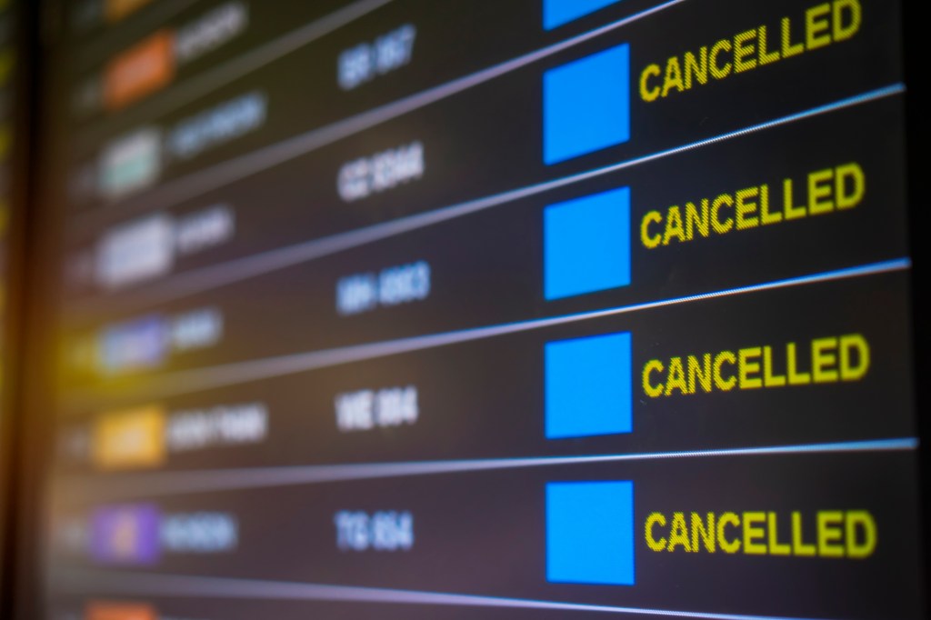 A close-up of an airport departure board showing multiple flights with the status "CANCELLED" in yellow text.