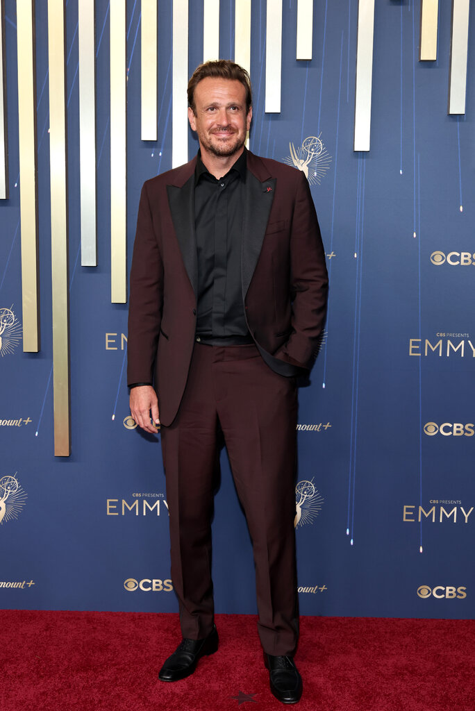 A man in a maroon suit stands with one hand in his pocket.