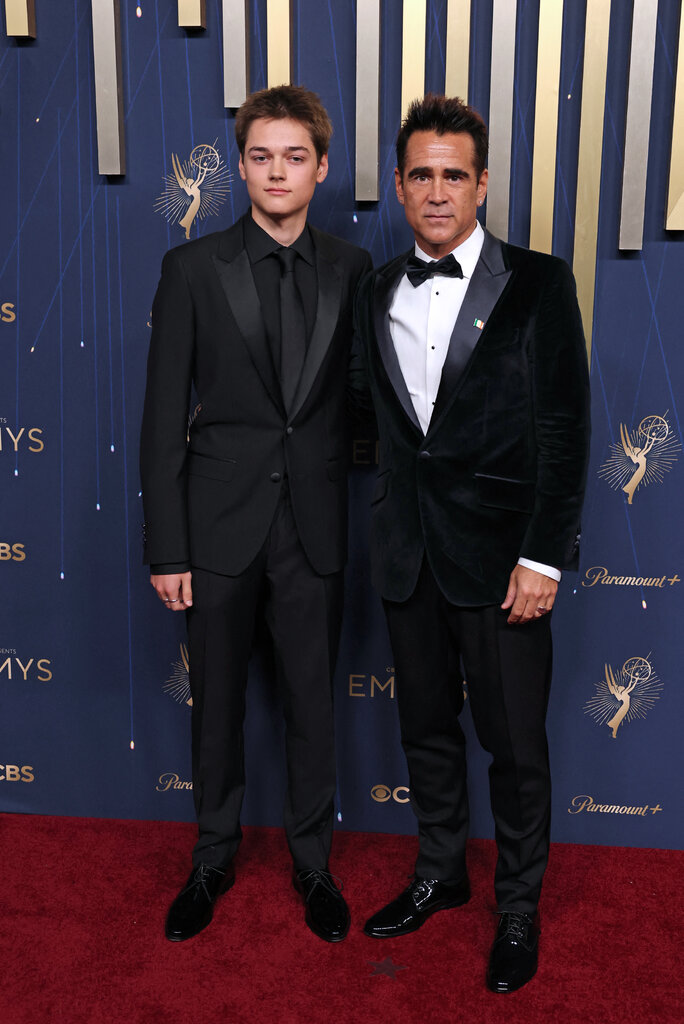 A man in a black suit and tie (left) stands next to a man in a navy tuxedo.
