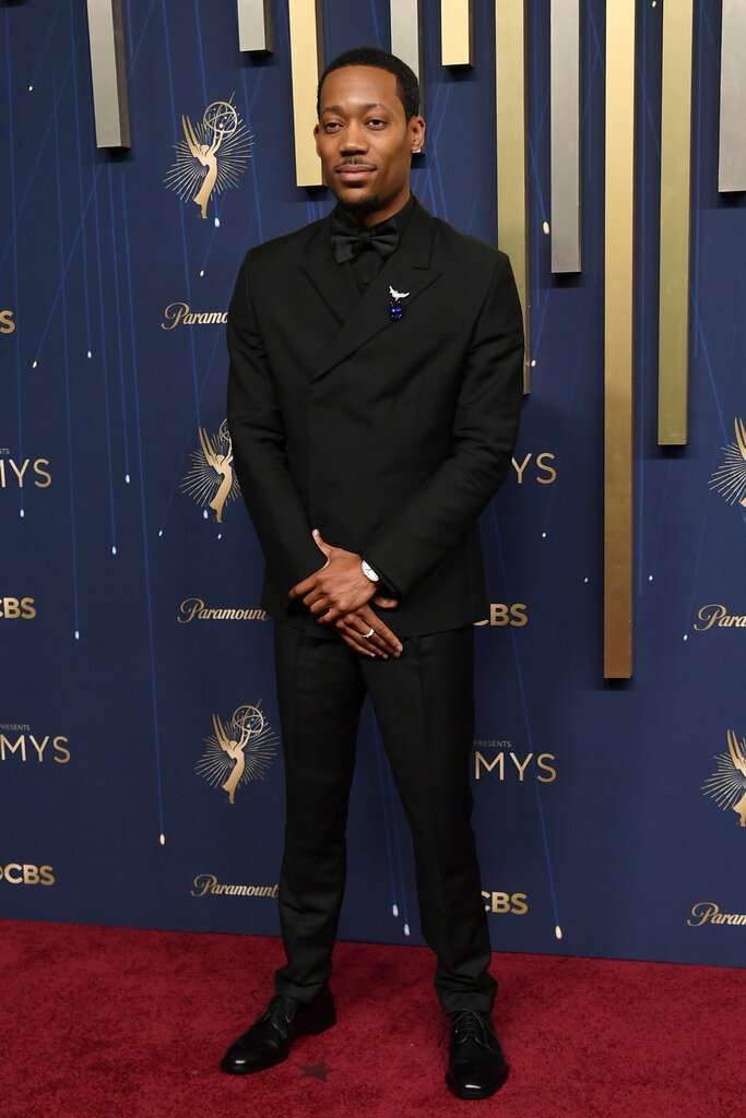 A man wearing a black tuxedo poses with his arms crossed.