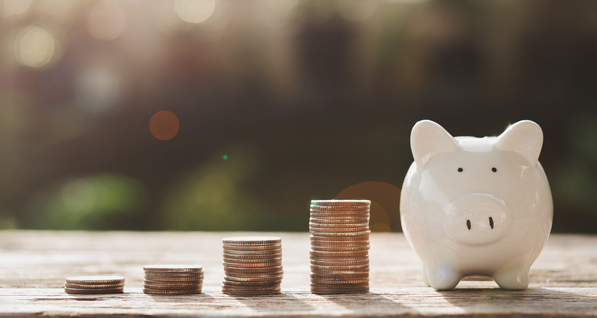 Four stacks of coins growing in size from left to right with a piggy bank at the end.