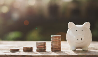Four stacks of coins growing in size from left to right with a piggy bank at the end.
