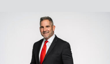 Grant Cardone smiling in a suit with a red tie