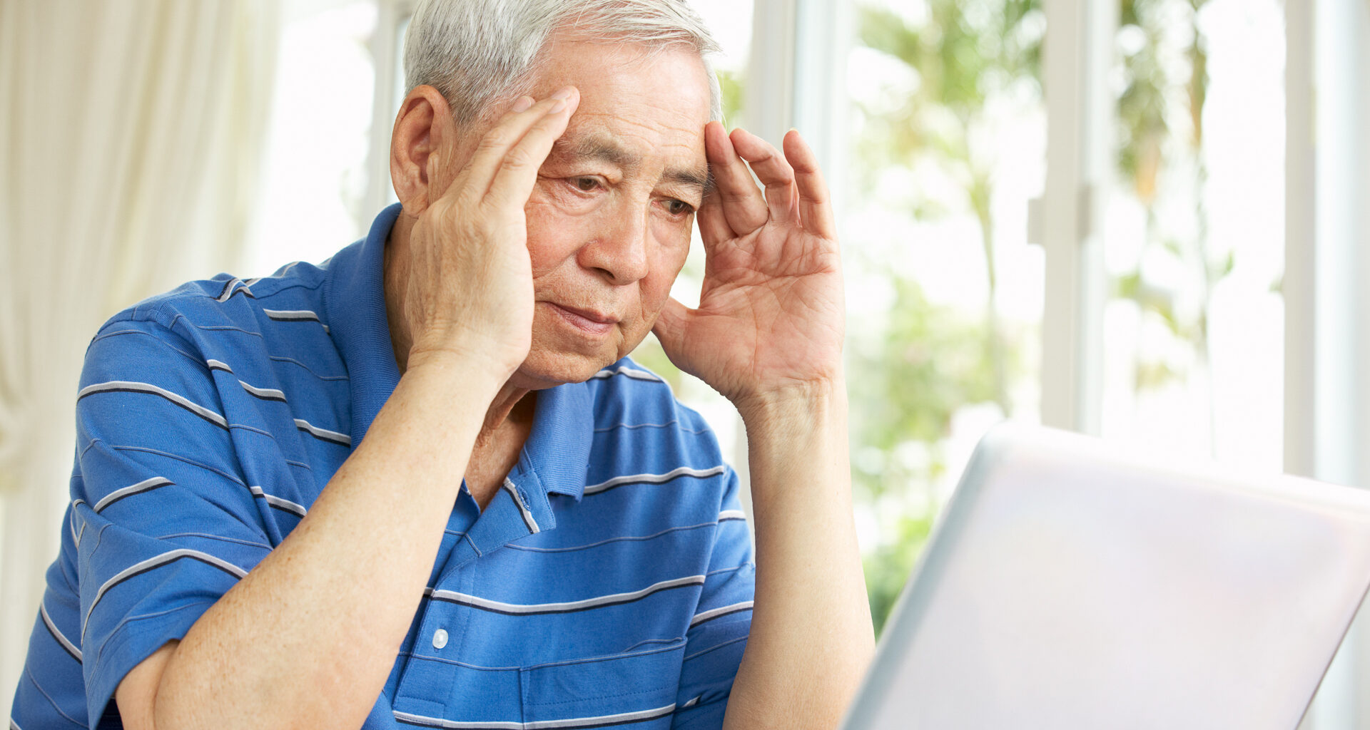 An older man sitting at a laptop looking worried