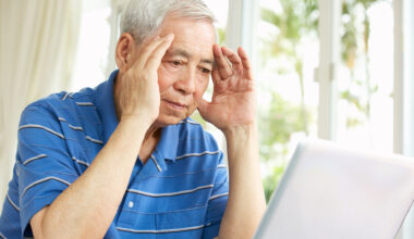 An older man sitting at a laptop looking worried