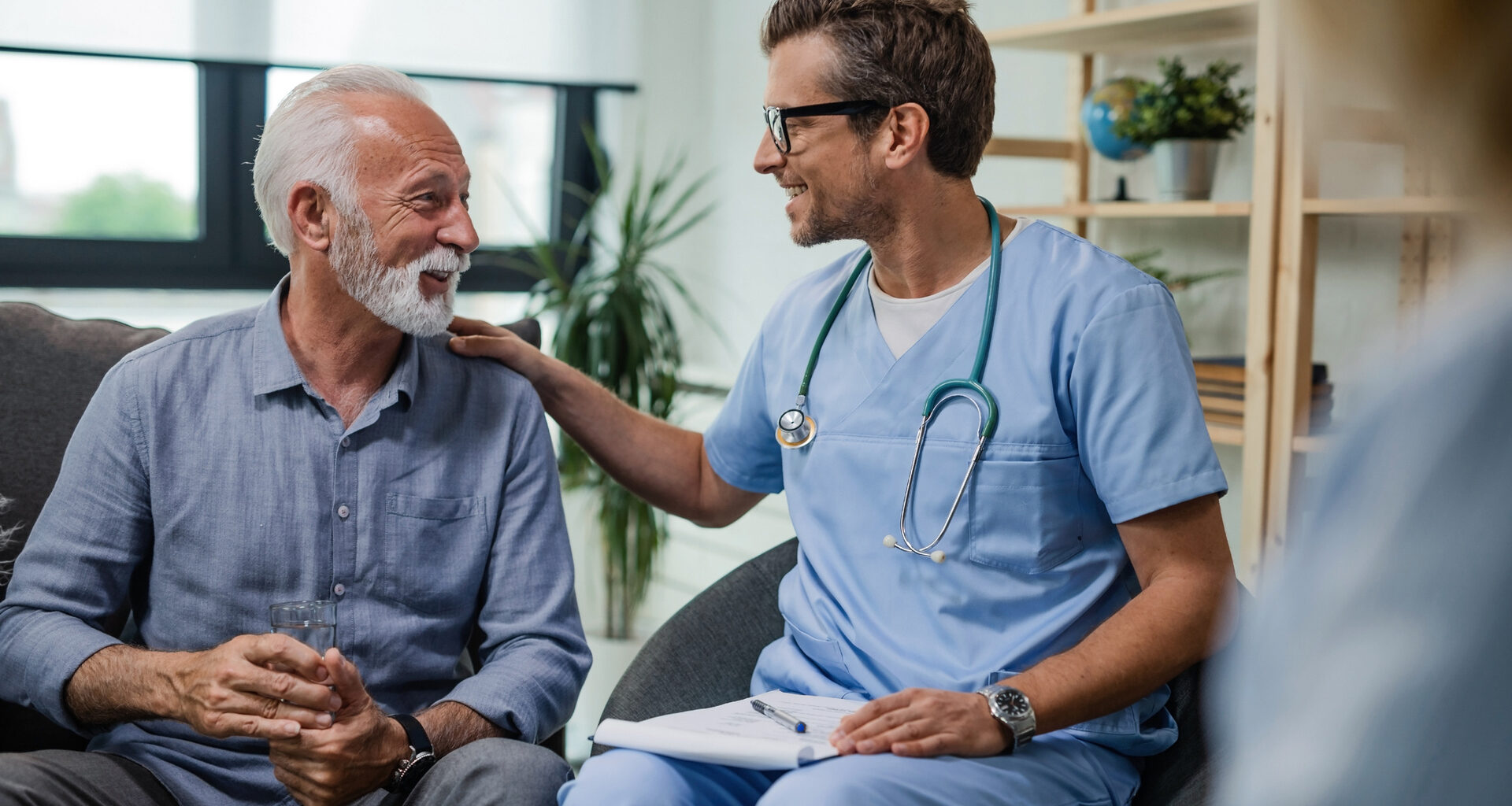 Happy doctor talking to senior male patient while being in a home visit.