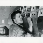 A man lifting a piece of wood and sticking out his tongue.