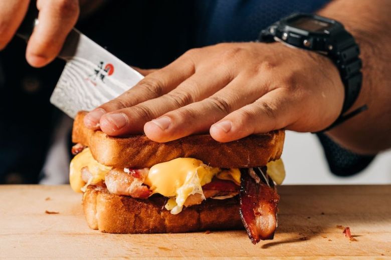 Chef Matthew Garcia's hands cut into a bacon, egg & cheese sandwich.