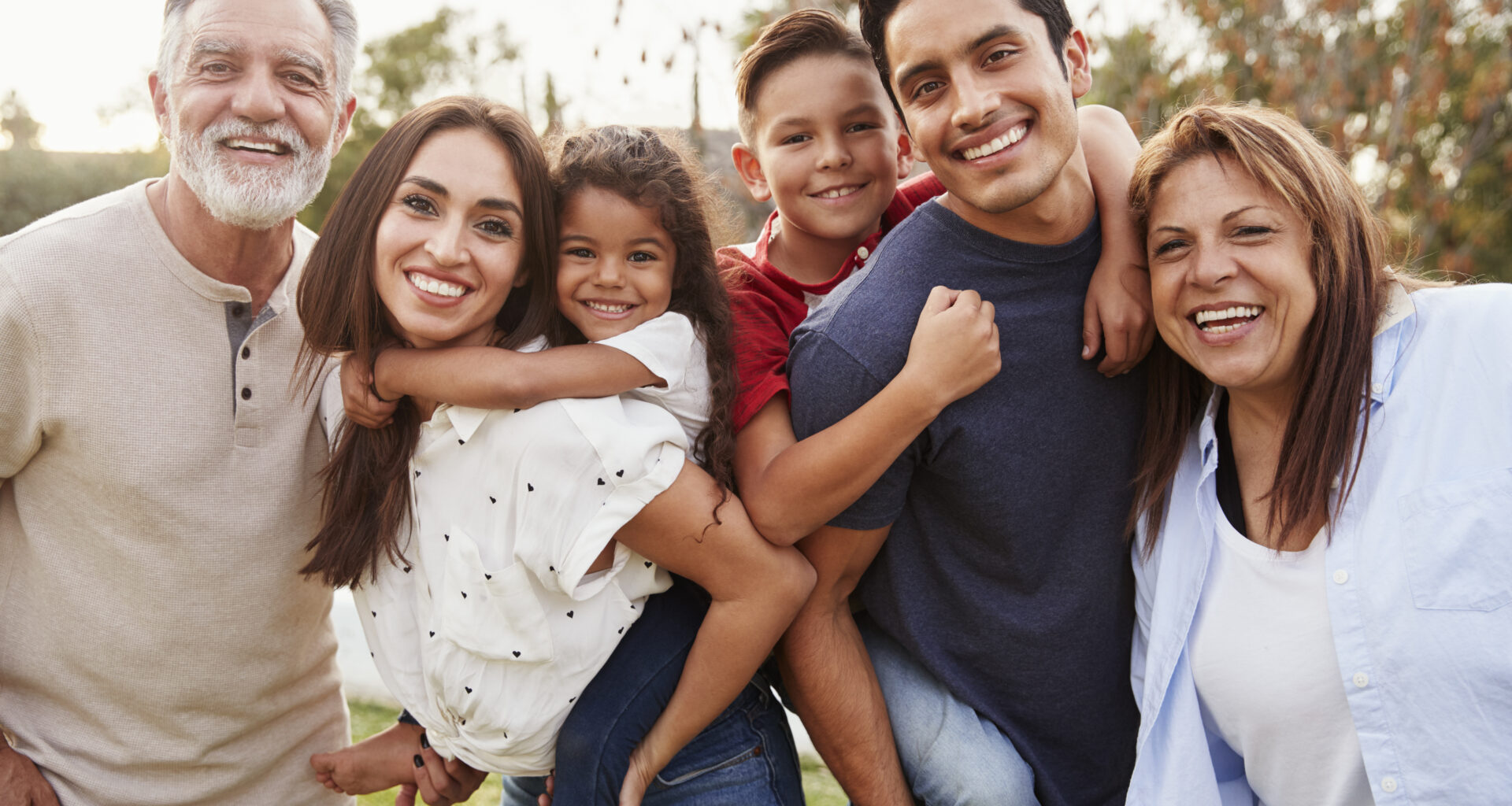 Three generation Hispanic family standing in the park, smiling to camera, selective focus