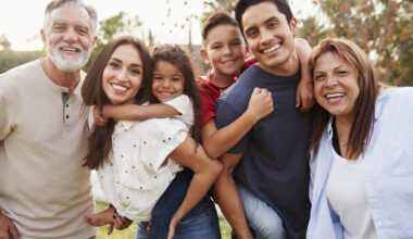 Three generation Hispanic family standing in the park, smiling to camera, selective focus