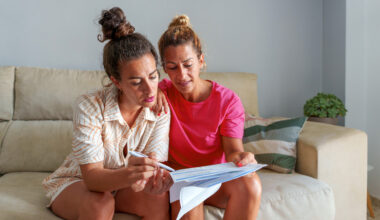 Women looking at bills on a couch.