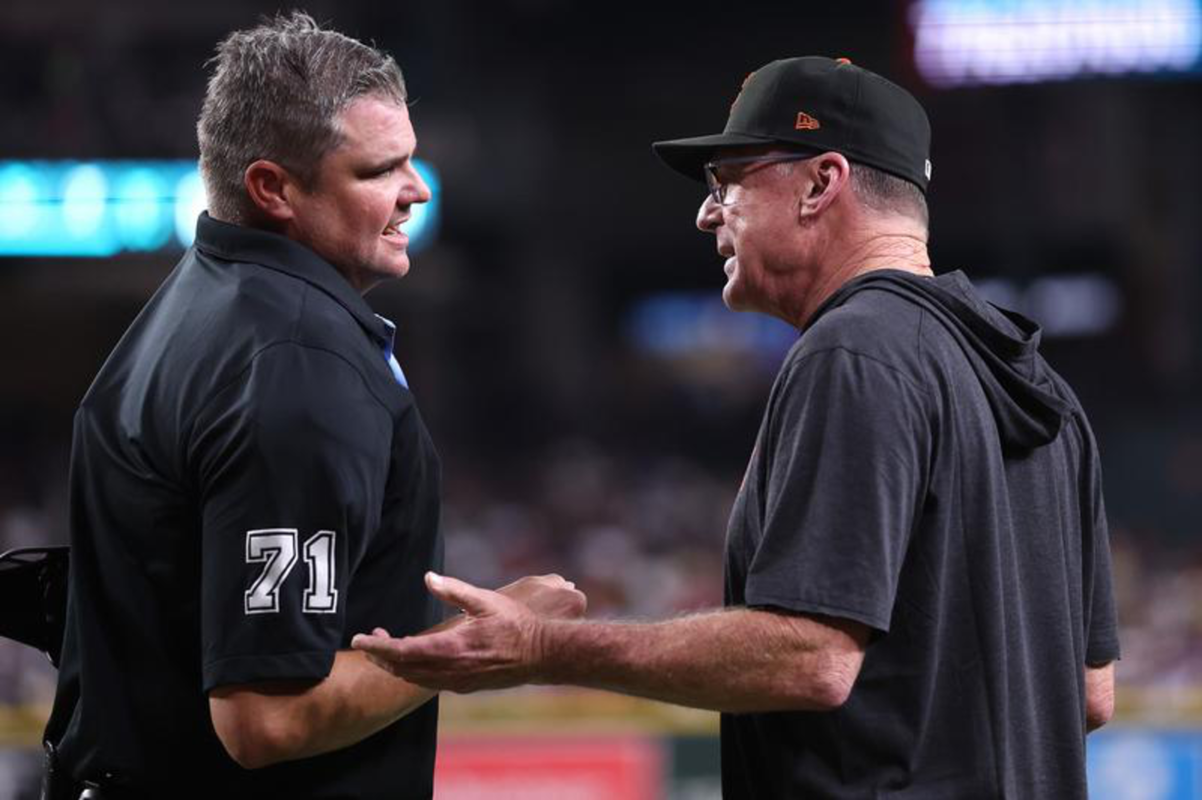 Two men are engaged in a conversation, one wearing a black shirt with “71" on the sleeve, the other in a black cap and hoodie.