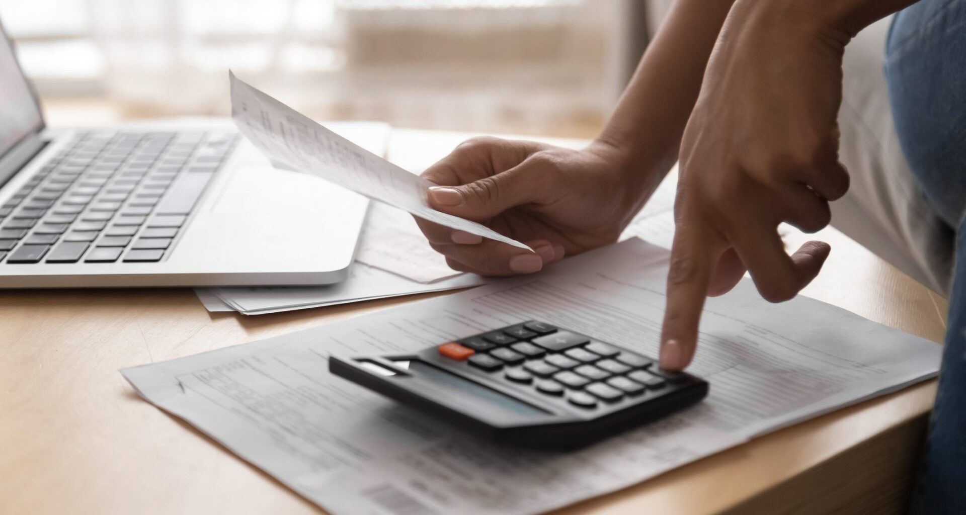 African woman holding in hand paper bills bank receipt using calculator on table calculate debt loan tax cost to pay manage finances concept doing accounting paperwork budget analysis, close up view.