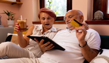A lovely senior couple sits together in their cozy living room, using a tablet for online shopping.