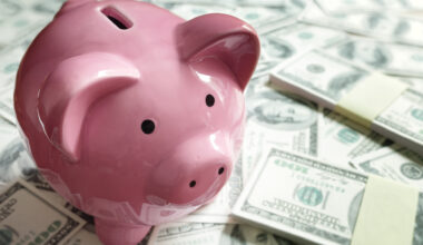 A pink piggy bank standing on top of a pile of cash.
