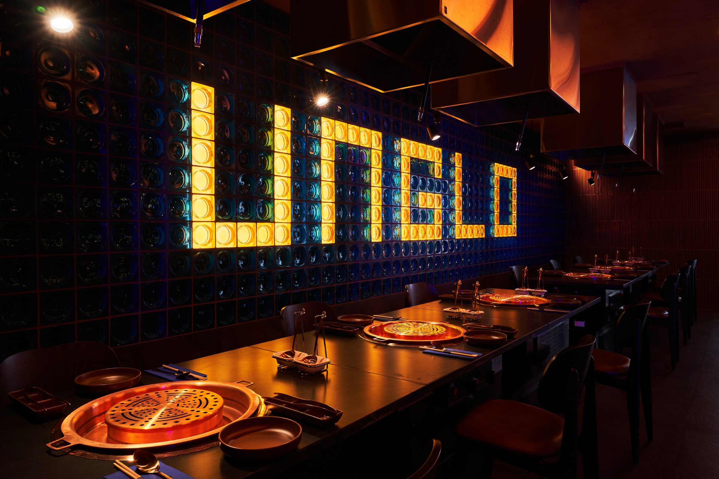 A long table at a restaurant with grills in the middle and a lit-up sign on the wall reading Unglo.