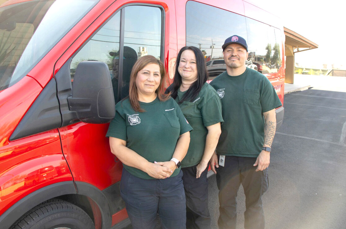 Mary Prado, left, and two other crisis intervention specialists with the Phoenix Community Assistance Program, which provides mental health specialists to respond to emergency calls instead of or in addition to police, pose for a photo in front of a van.