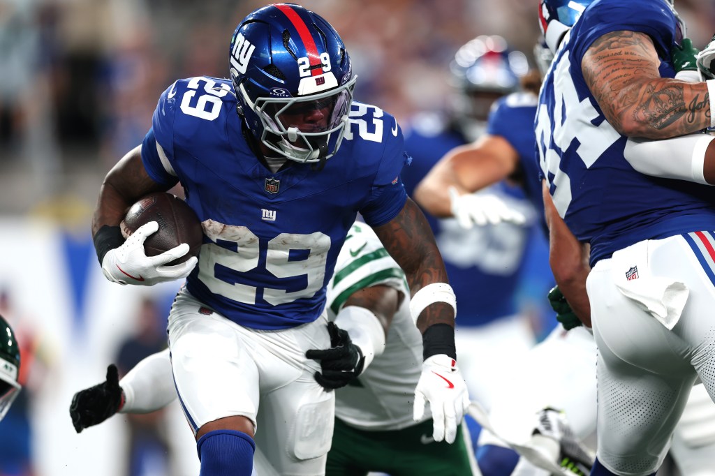 New York Giants player running with the football during a preseason game.
