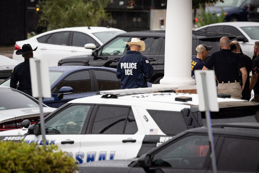 ICE, police, and FBI investigators take shelter from the rain under a building overhang in a...