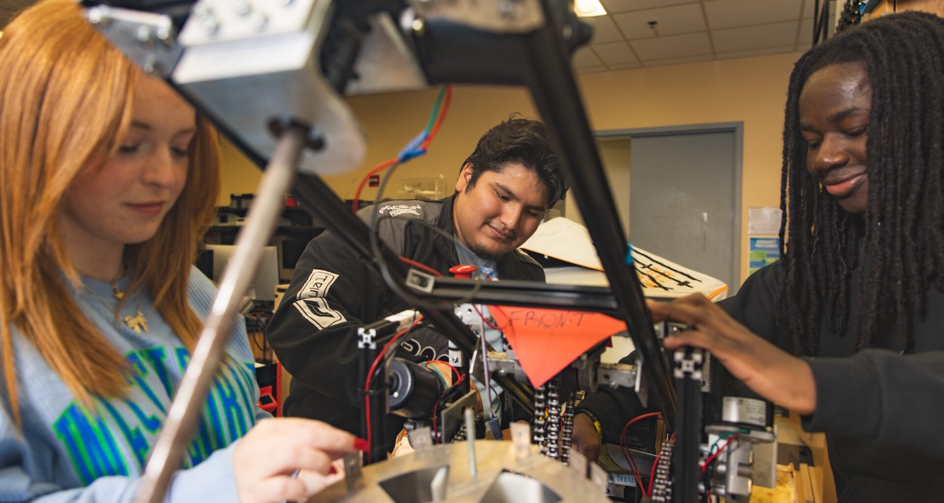 Three University of West Florida students sitting at desk working on mechanical robot arm.