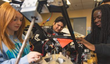 Three University of West Florida students sitting at desk working on mechanical robot arm.