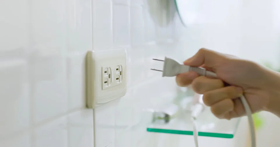 Hand plugging an electrical cord into a wall outlet in a modern room
