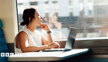 Young business woman looks out the train window while using her laptop on a table