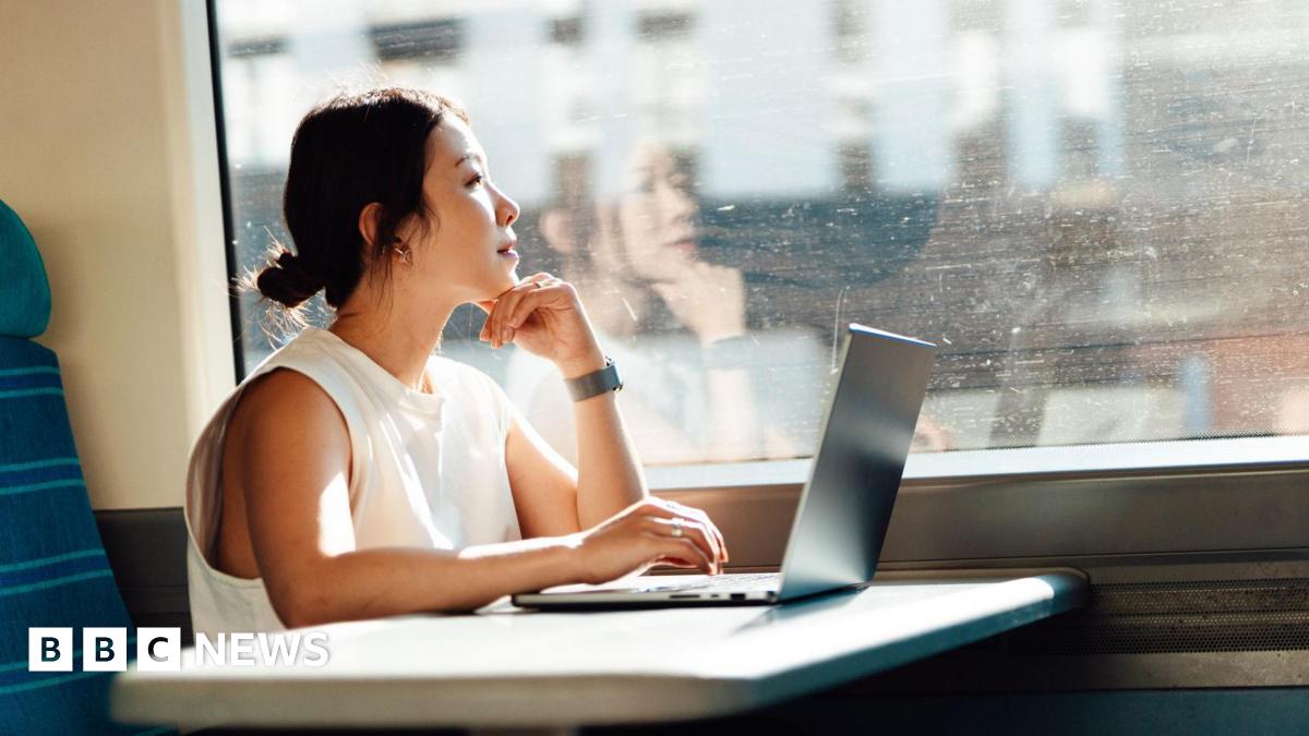 Young business woman looks out the train window while using her laptop on a table