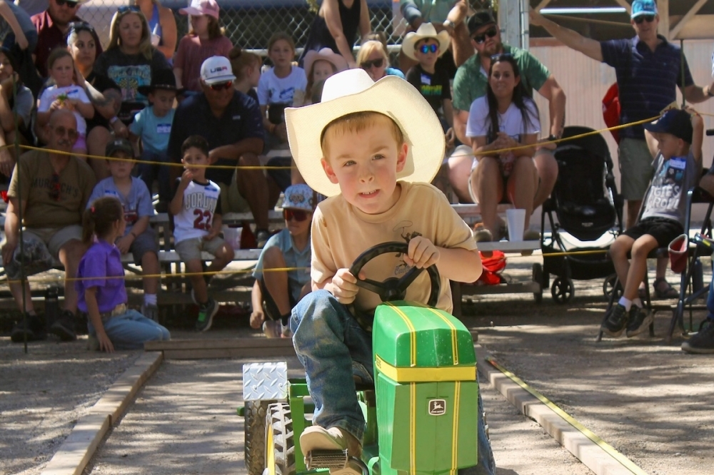 A child rides a toy tractor at a race at the county fair.