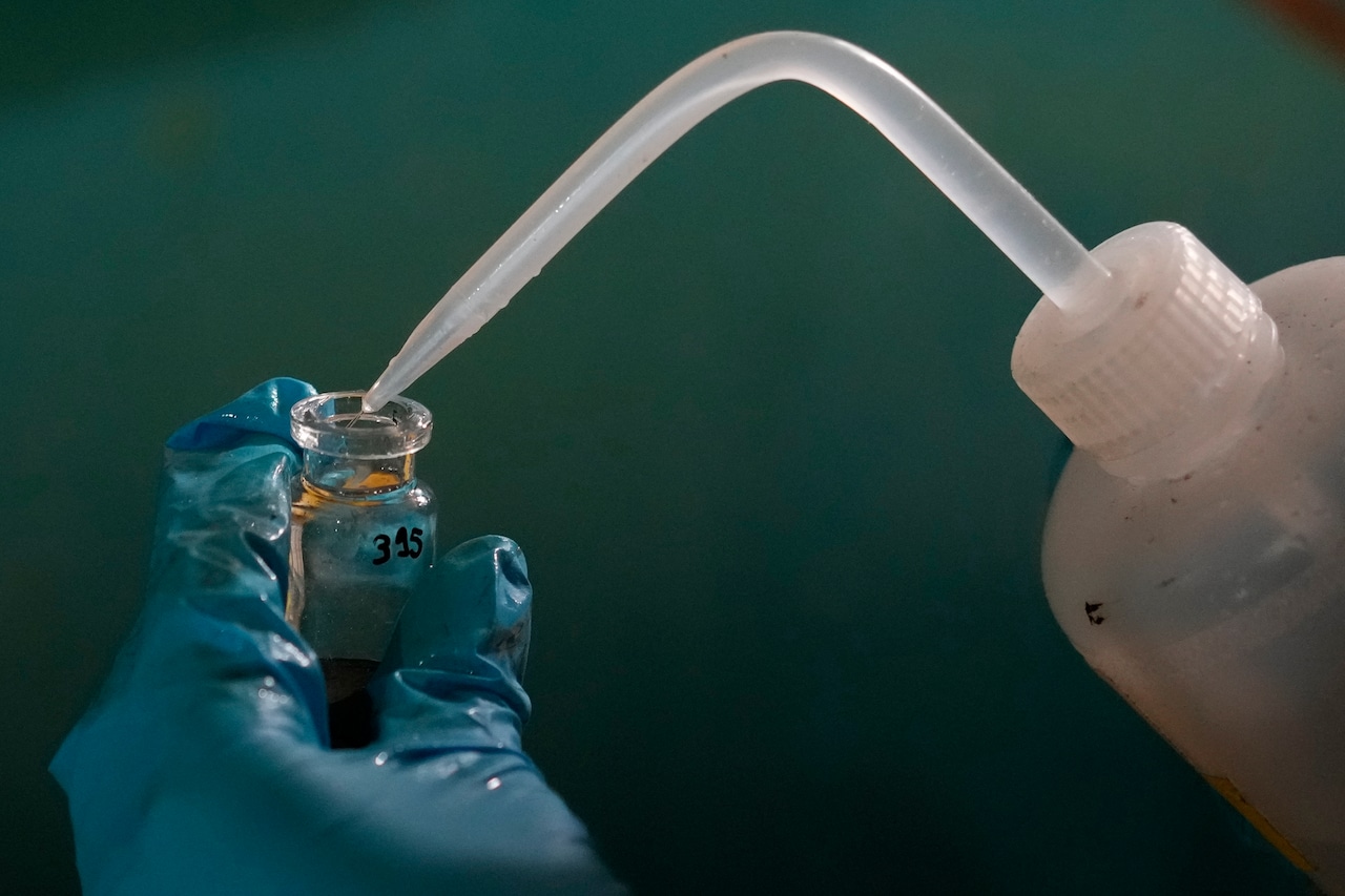 A hand holds up a vial with a squeeze bottle with tube attached pointing into it.