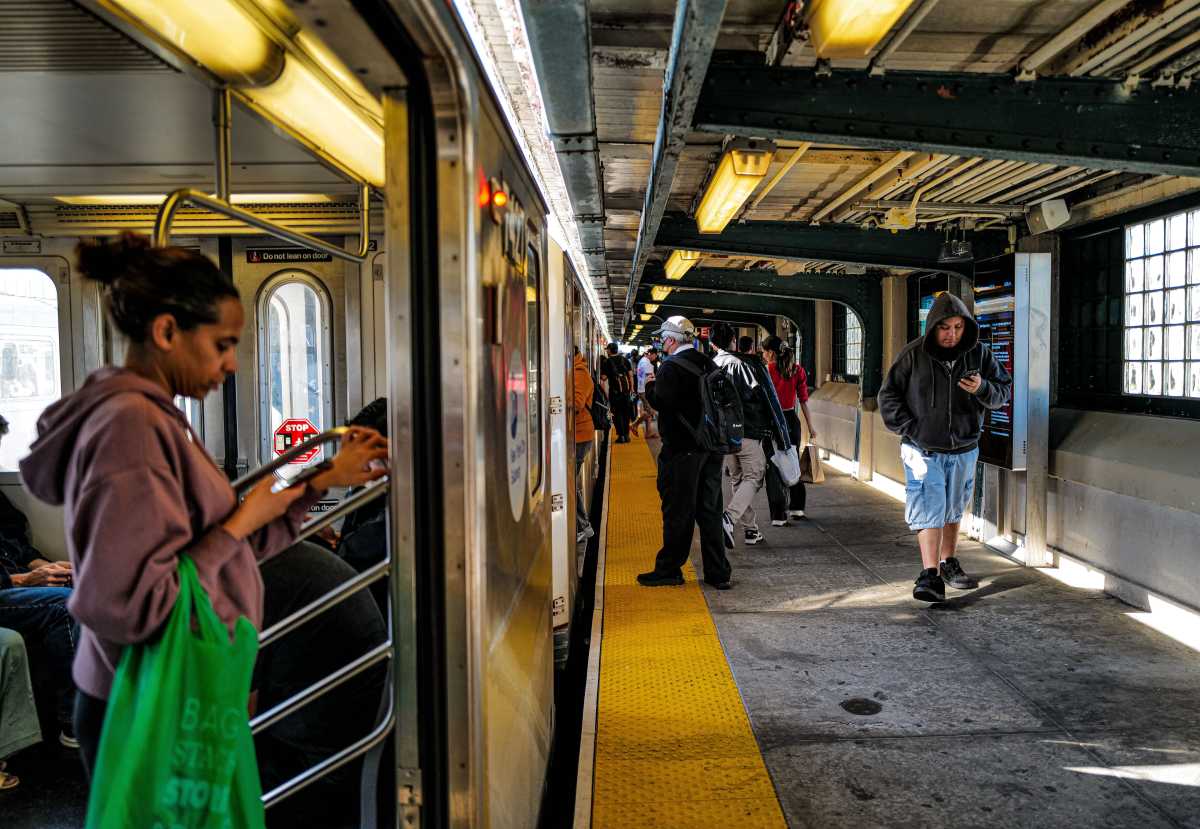 Commuters on board a stopped 7 train and walking on a platform in Queens on Oct. 22, 2024.