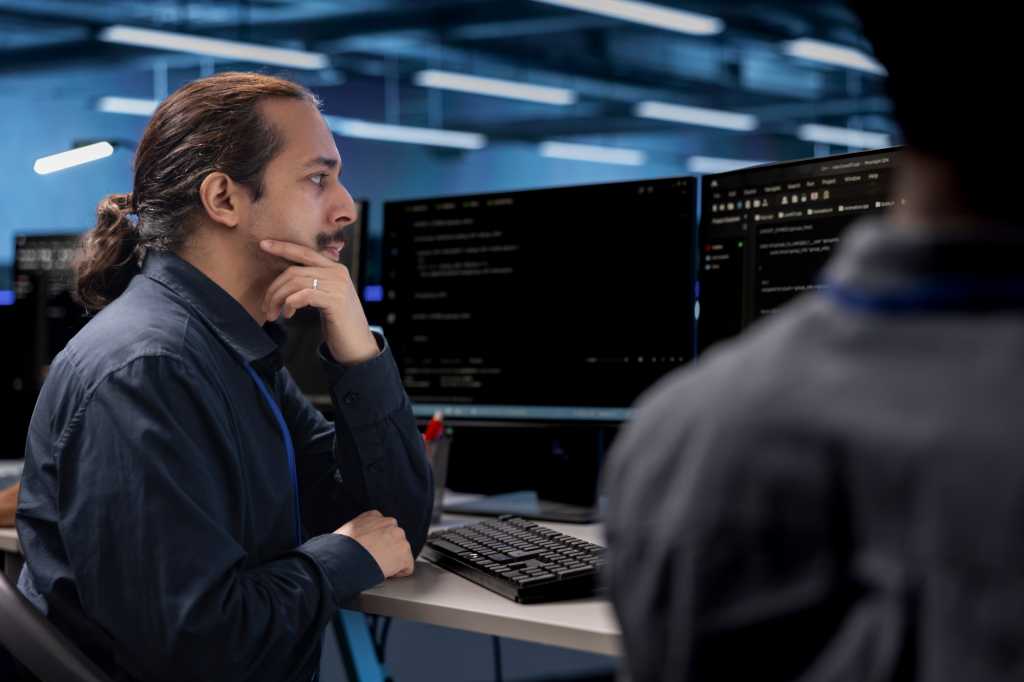 Admin in data center updating systems, protecting hardware equipment from damaging software vulnerabilities. Colleagues looking for bugs causing infrastructure to slow down