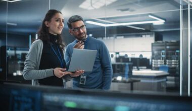 Portrait of Two Happy Female and Male Engineers Using Laptop Computer to Analyze and Discuss How to Proceed with the Artificial Intelligence Software. Casually Chatting in High Tech Research Office
