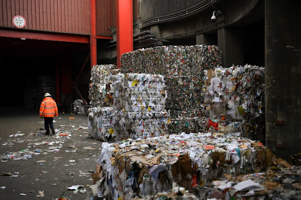 A man walks next to piles of compressed plastic and papers at the recycling department of the Cory Western Riverside facility, part of the Cory Riverside Energy, in Wandsworth, in London, on January 18, 2022. - Cory Riverside Energy has evolved from a coal distribution company end of the 19th century into a recycling and waste management structure. The waste is transported by boat in four riverside waste plants along the Thames. The Western Riverside facility sorts and segregates dry mixed recyclables, according to its last figures, the structure processed 71,000 tones of dry mixed recyclables. (Photo by Daniel LEAL / AFP) (Photo by DANIEL LEAL/AFP via Getty Images)