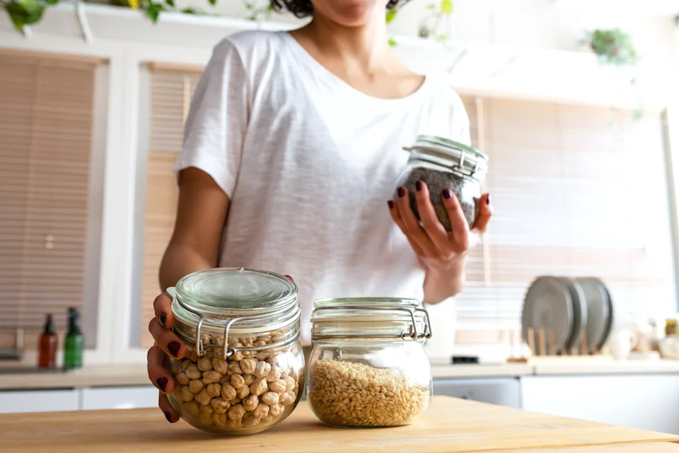 Person in a kitchen holding a jar of lentils, with other jars of grains on the counter, suggesting organization and meal prep