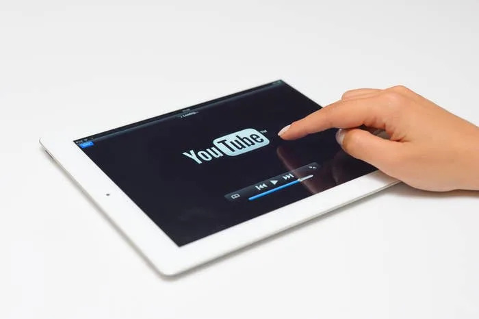 A hand is about to press play on a video from the YouTube app displayed on a tablet screen