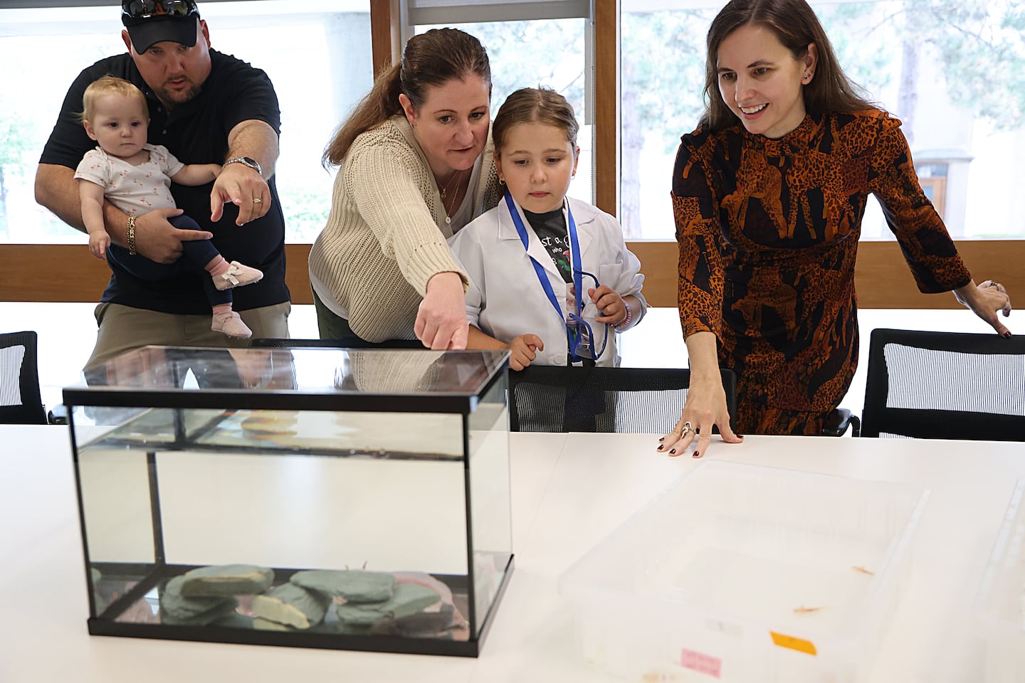 At the Harvard Department of Stem Cell and Regenerative Biology, 6-year-old Marianne Cullen (in lab coat) examines axolotls in the lab of Jessica Whited, who is on the far right.  Behind her is her father, Robert Cullen, baby sister Emmaline Cullen, and mother Kat Demetrion.