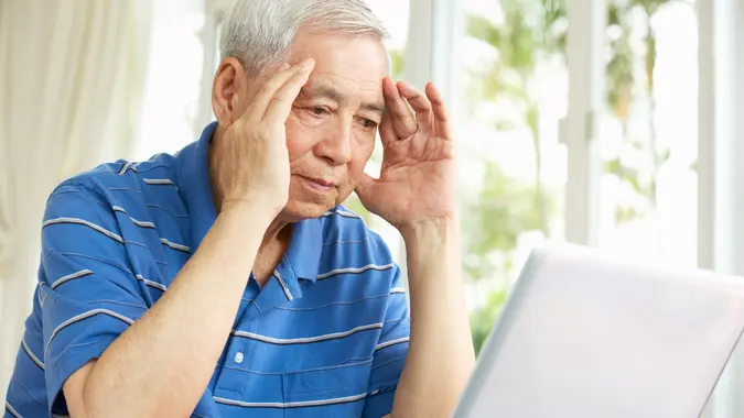 An older man sitting at a laptop looking worried