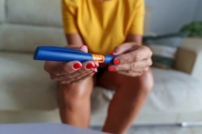 Person holding an insulin pen while sitting on a couch, focusing on the pen