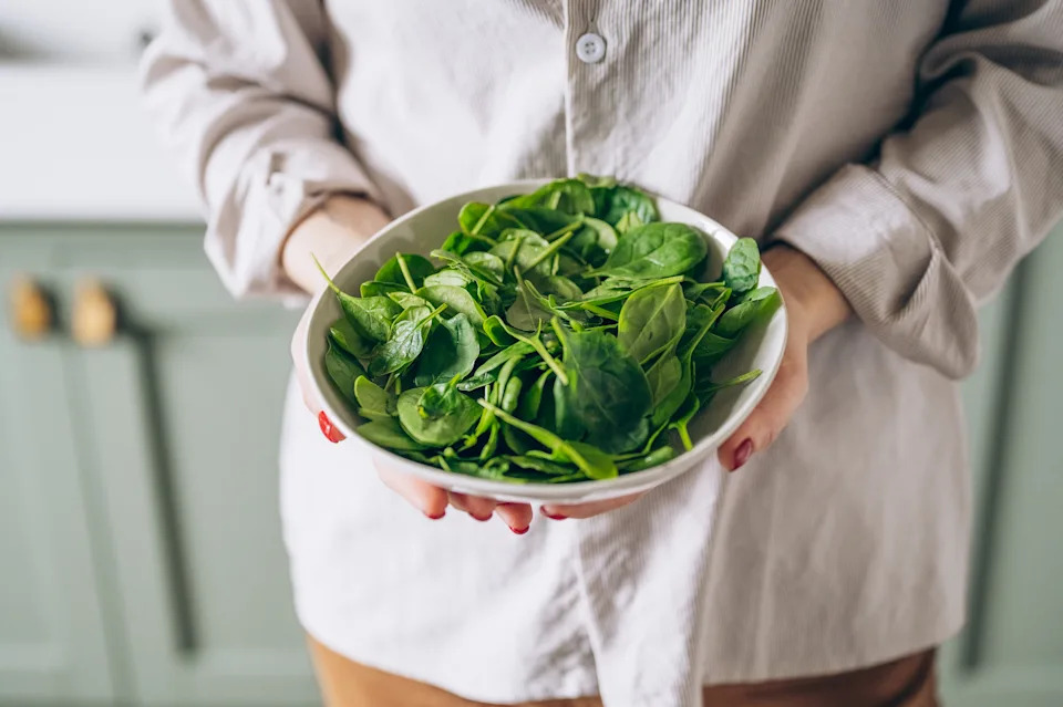 Green vegan breakfast meal in bowl with spinach, arugula, avocado, seeds and sprouts. Girl in leggins holding plate with hands visible, top view. Clean eating, dieting, vegan food concept