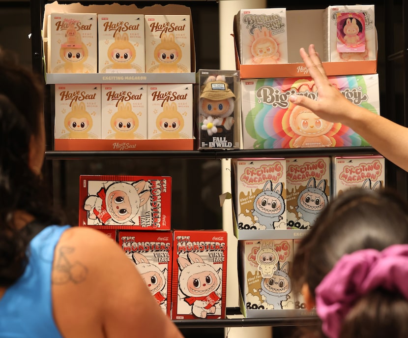 A booth vendor directs fans through a variety of items on display for sale at the Labubu...