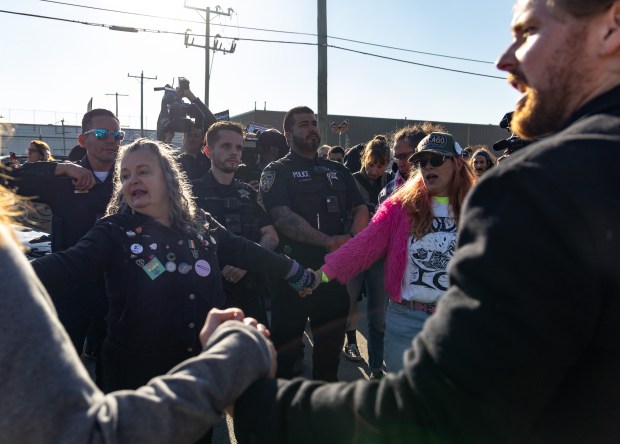 Protesters and activists sit and join hands in front of...