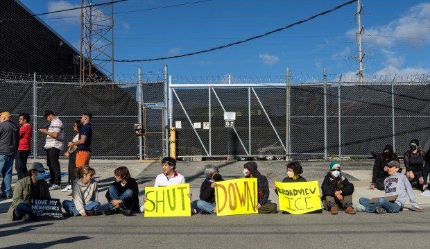 Protesters and activists sit in front of a gate to...