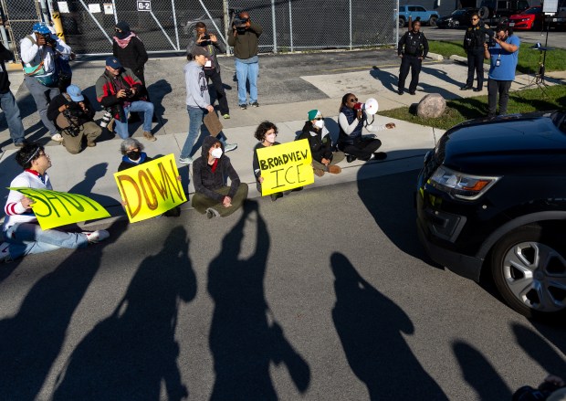 Protesters and activists sit in front of a federal agent’s...