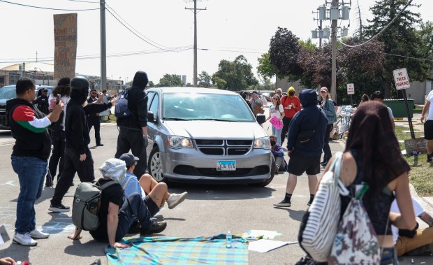 Vehicles with federal agents drive close to protesters attempting to...