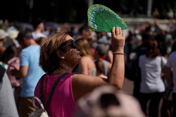 FILE - A tourist uses a fan to shade her face from the sun while waiting to watch the Changing of the Guard ceremony outside Buckingham Palace, during hot weather in London, July 18, 2022. (AP Photo/Matt Dunham, File)